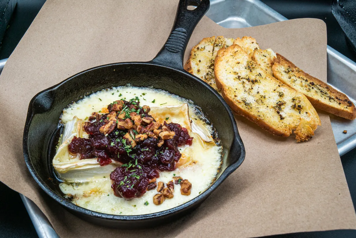 A baked skillet dip topped with cranberry, served with toasted garlic bread