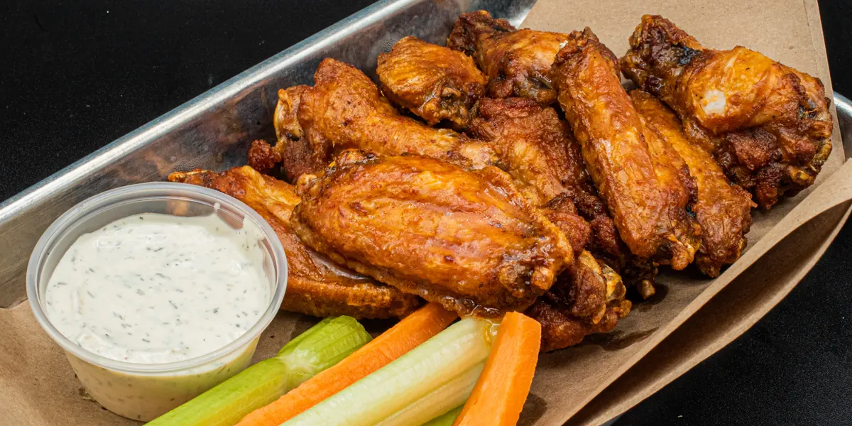 A tray of Perfect SZN chicken wings with dip and veggie sticks